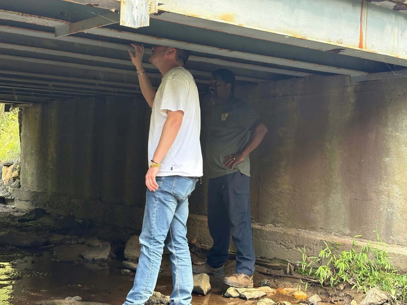 Mayor Holland Perdue reaches up to the steel beams under the bridge while a town worker looks on.